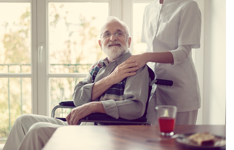 Senior patient in nursing home with helpful nurse in white uniform