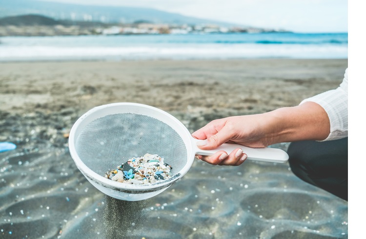 Young woman cleaning microplastics from sand on the beach - Environmental problem, pollution and ecolosystem warning 
