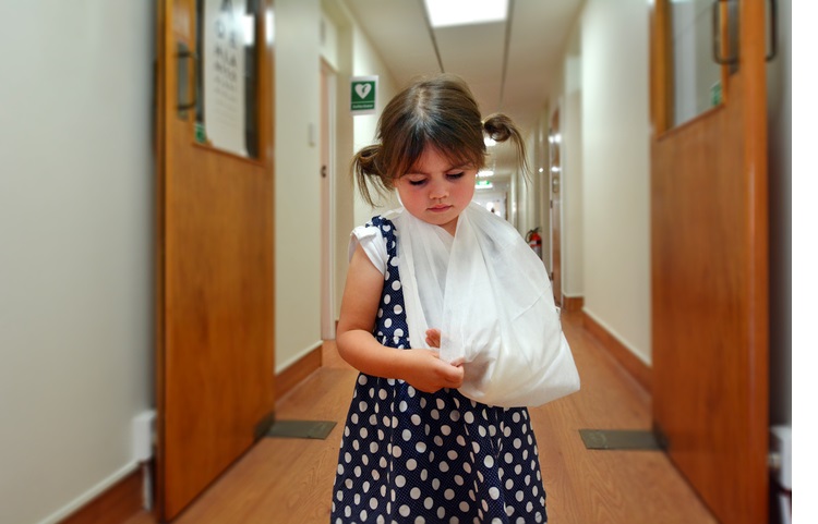Sad little girl with a broken arm in hospital corridor