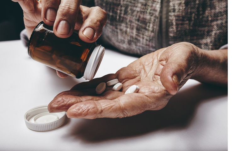 Close-up image of senior woman taking out pills from the pills bottle. Focus on hands. Old female taking medicines.