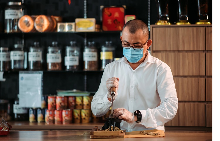 Asian chinese male pharmacist cutting chinese herbs in front of counter at chinese medicine shop