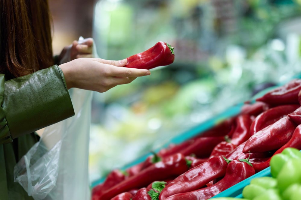 Frau hält im Supermarkt eine rote Paprika in ihrer Hand