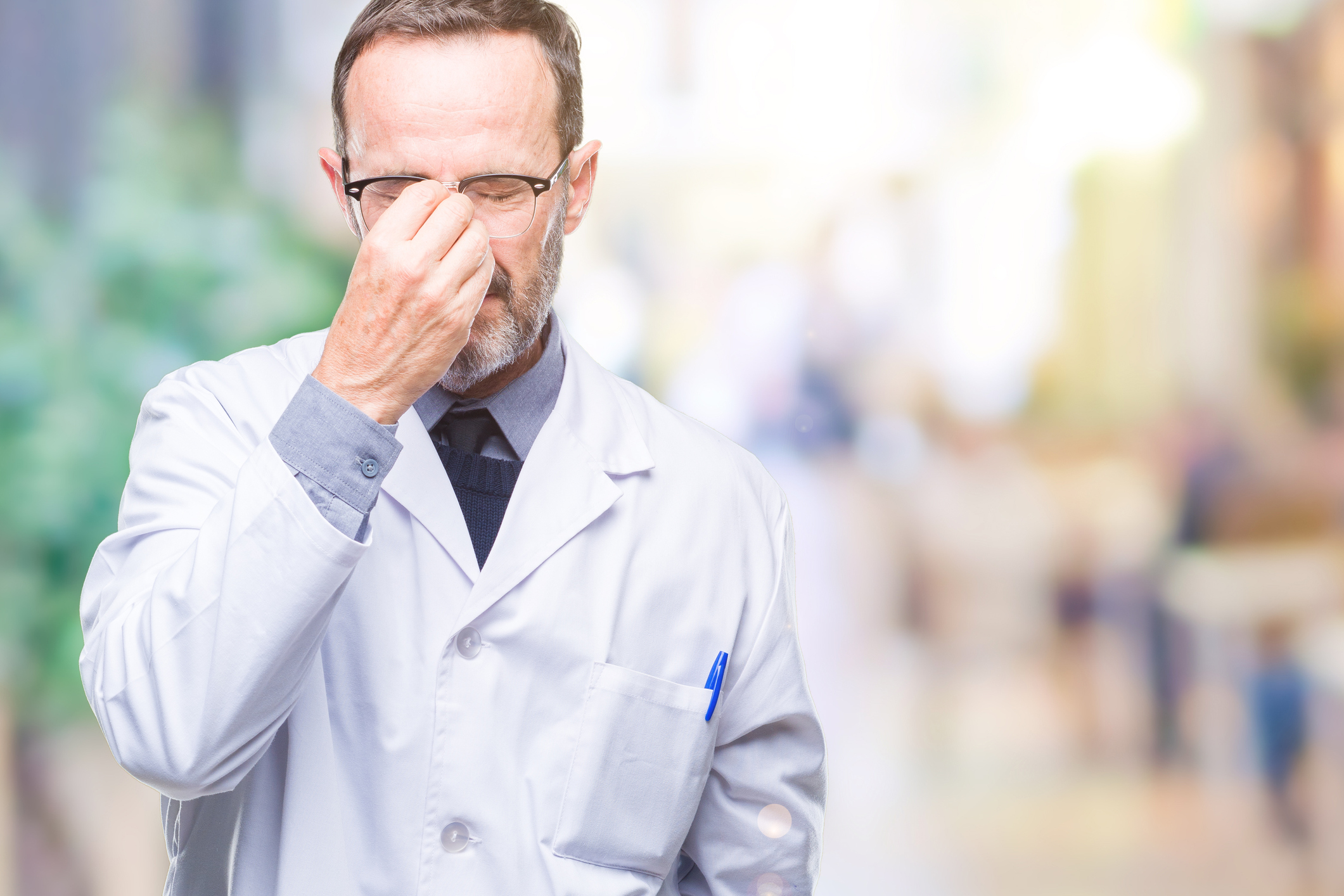 Middle age senior hoary professional man wearing white coat over isolated background tired rubbing nose and eyes feeling fatigue and headache. Stress and frustration concept