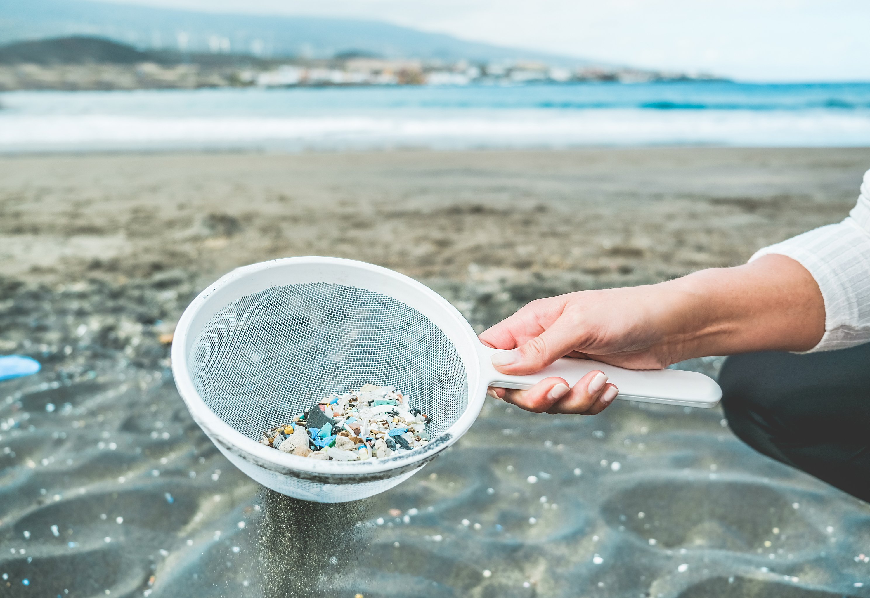 Young woman cleaning microplastics from sand on the beach - Environmental problem, pollution and ecolosystem warning 