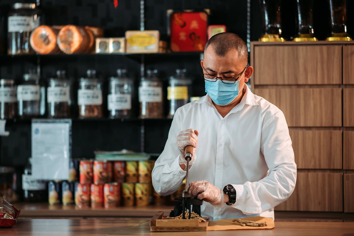 Asian chinese male pharmacist cutting chinese herbs in front of counter at chinese medicine shop