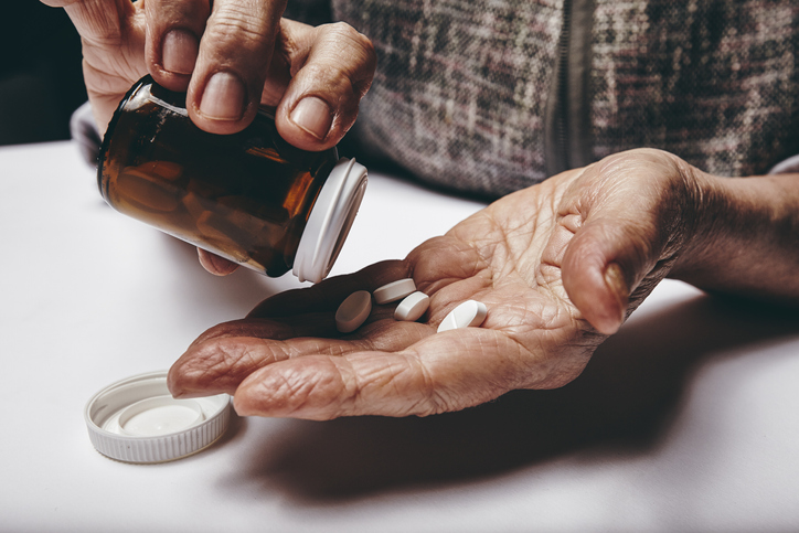 Close-up image of senior woman taking out pills from the pills bottle. Focus on hands. Old female taking medicines.