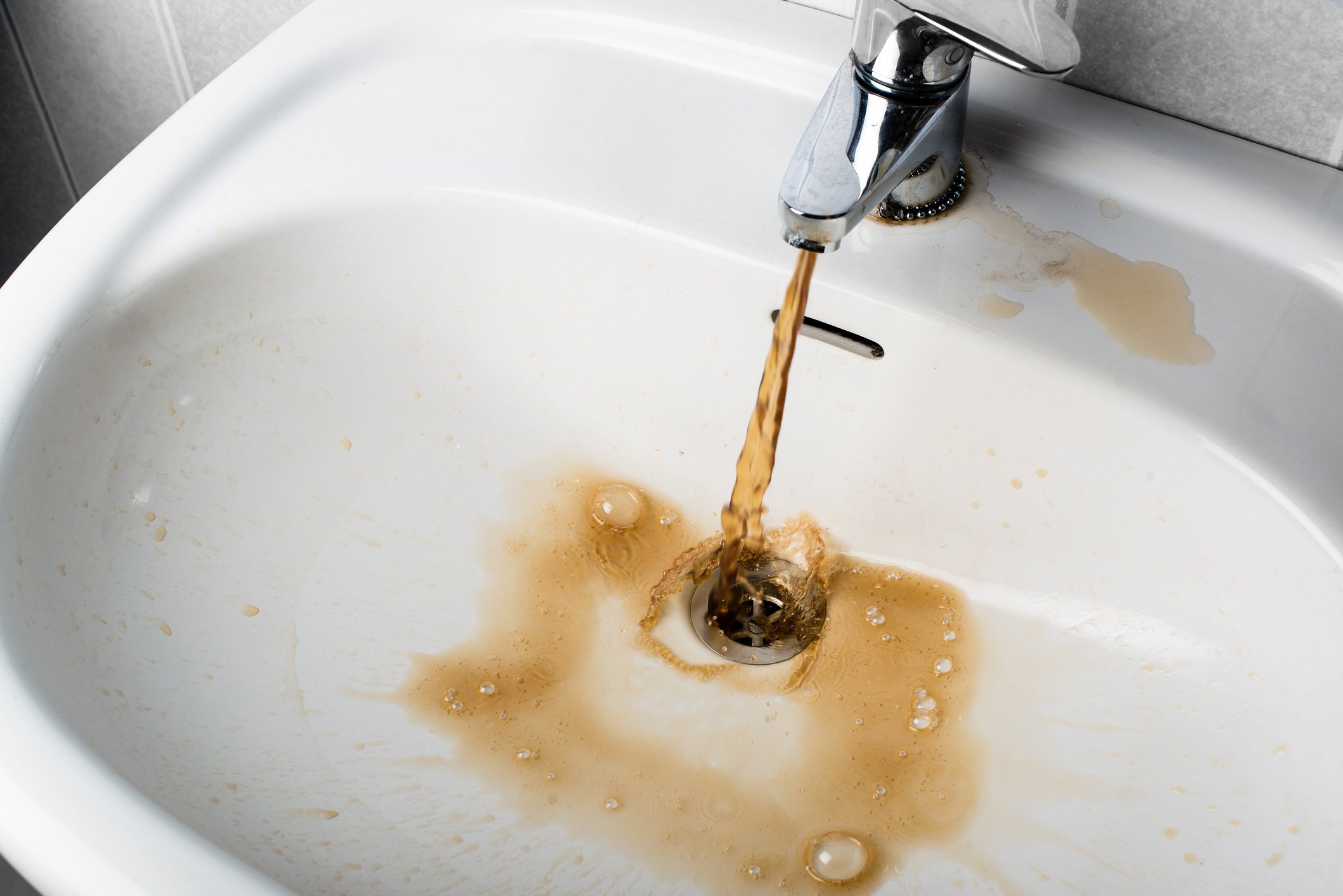 Dirty brown water running into a white sink