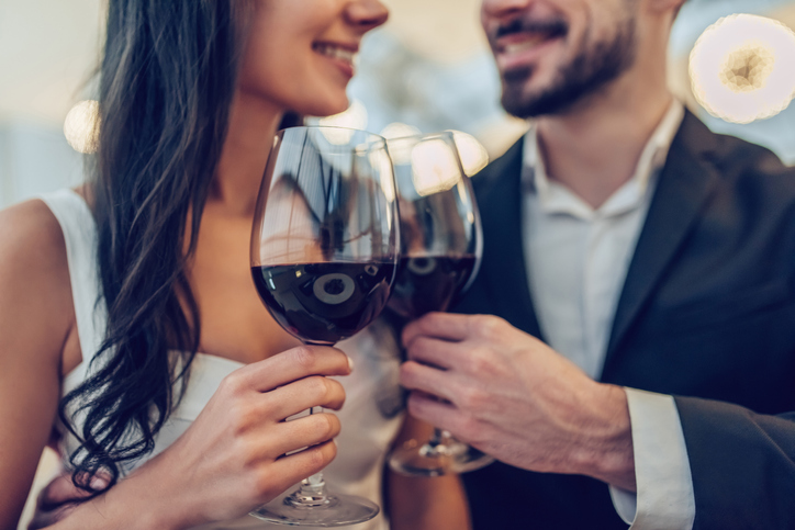 Cropped image of loving couple is spending time together in modern restaurant. Attractive young woman in dress and handsome man in suit are having romantic dinner. Celebrating Saint Valentine's Day.